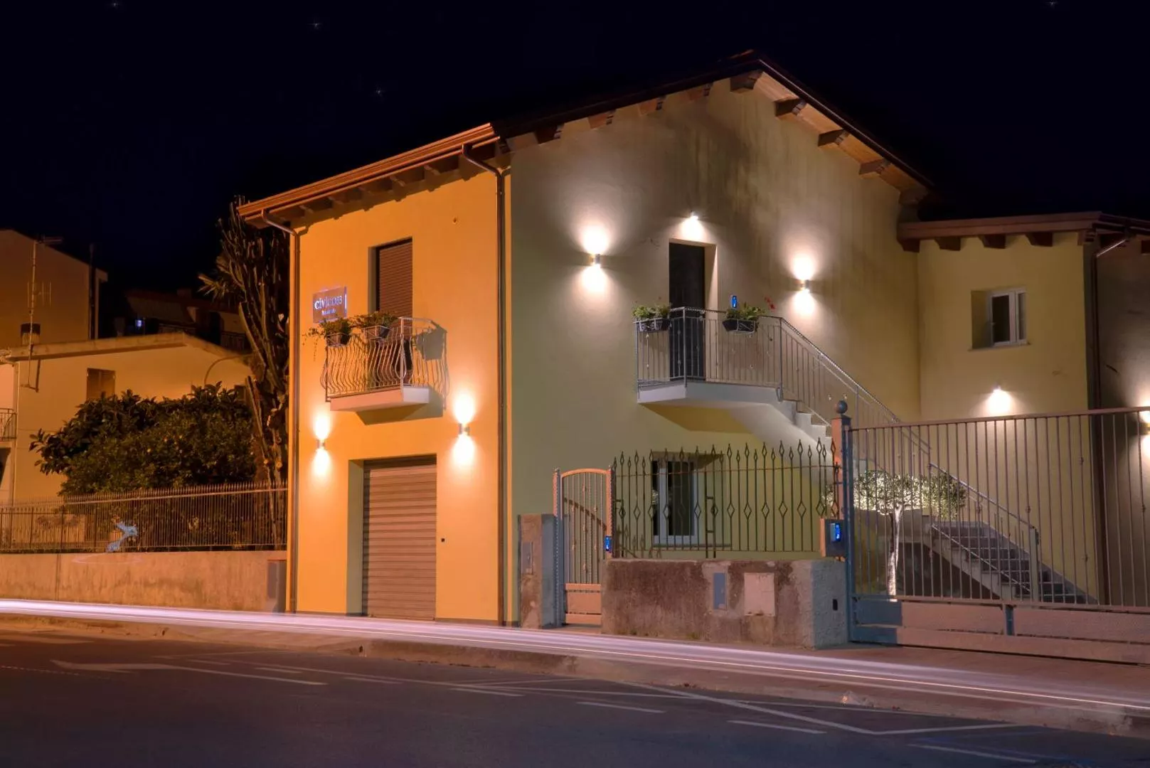 La facciata del Civico 33 illuminata di sera, con la scala esterna e il cancello